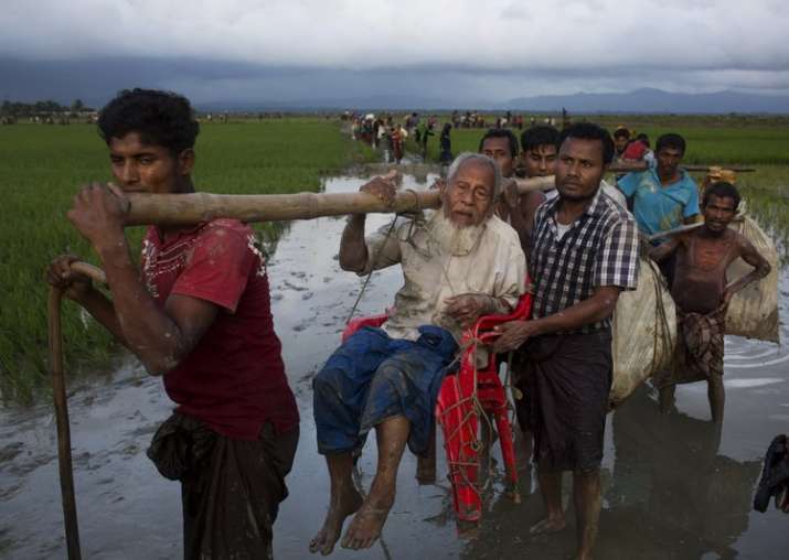 Ethnic Rohingya carry an elderly man and walk through
