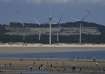 Beachgoers walk near wind turbines along the coast of