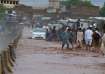 People wade through a flooded bridge on a stream, which is overflowing following heavy rains, on the