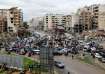 People gather as vehicles drive near damaged buildings, in Beirut's southern suburbs, after a ceasef