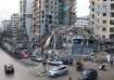 Vehicles drive past damaged buildings in Beirut's southern