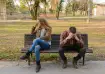 Couple sitting apart on a park bench after a breakup, looking upset and distant.