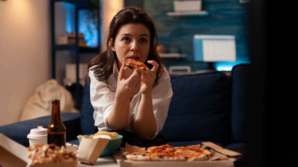 female holding delicious pizza slice eating takeaway food delivery while watching comedy