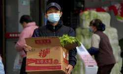 A man wearing a face mask carries a box with groceries as