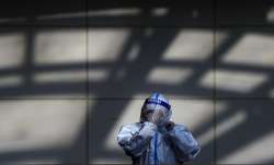 A worker in protective suit wipes his face shield at a