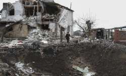 A woman stands on top of a crater next to a destroyed house
