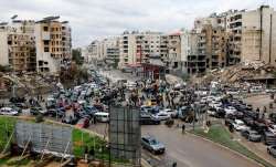 People gather as vehicles drive near damaged buildings, in Beirut's southern suburbs, after a ceasef