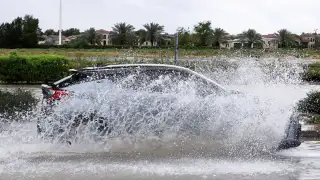 An SUV drives through floodwater covering a road i