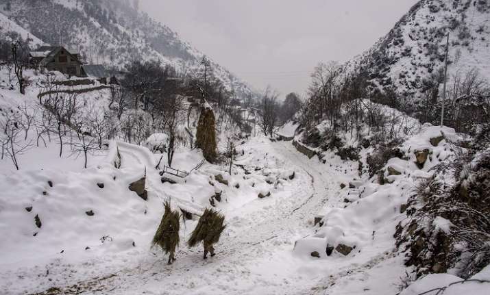 Villagers carry hay bales as they walk a snow-covered trail