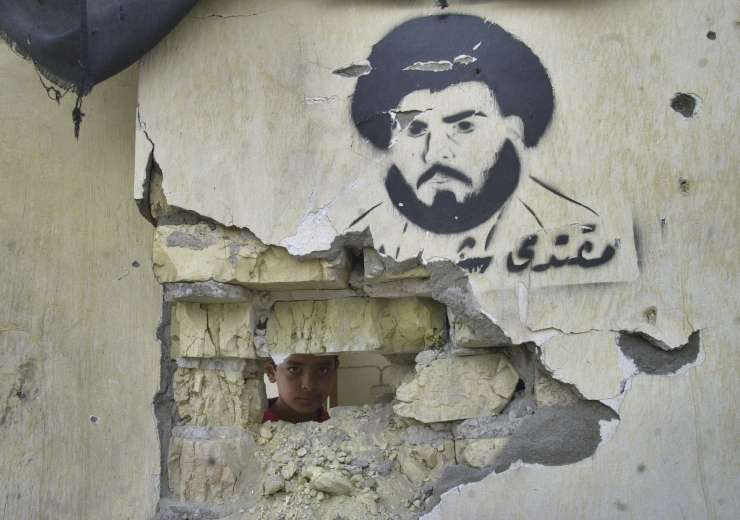 An Iraqi boy peers through a destroyed wall with a painting of militant Shiite cleric Moqtada al-Sadr in the Sadr City district in Baghdad, Iraq, Monday, May 10, 2004. - India Tv