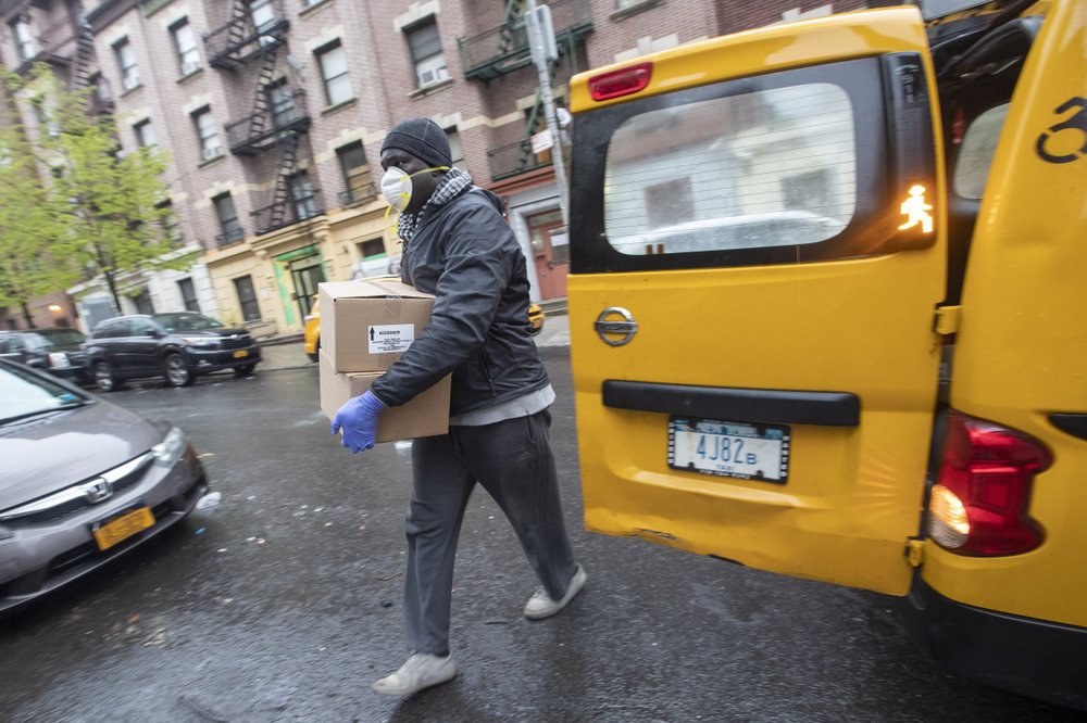 Taxi driver Mor Gob, wearing a mask to protect against coronavirus, delivers boxes with prepared meals to people in need in the Bronx borough of New York, Thursday, April 30, 2020. More than 3.8 million laid-off workers applied for unemployment benefits last week as the U.S. economy slid further into a crisis that is becoming the most devastating since the 1930s. (AP Photo/Mary Altaffer)