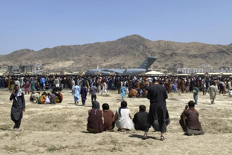 Hundreds of people gather near a U.S. Air Force C-17 transport plane at a perimeter at the international airport in Kabul, Afghanistan, Monday, Aug. 16, 2021.