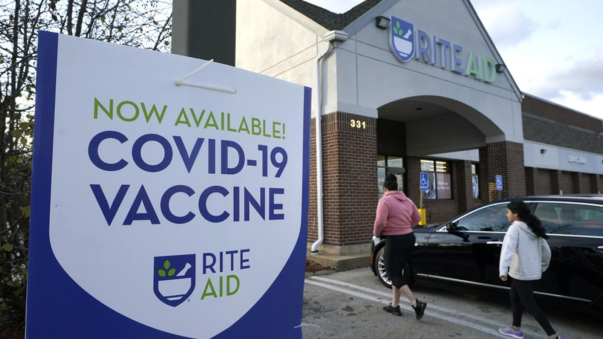 People walk past a COVID-19 vaccine sign as they enter a Rite Aid pharmacy, in Nashua, N.H.&nbsp;