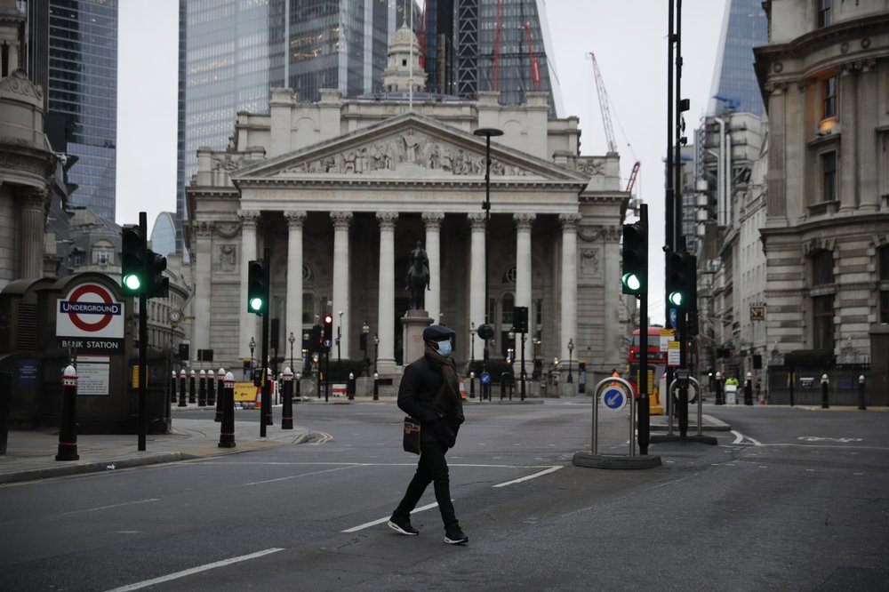 A man crosses the street backdropped by the Royal Exchange in the City of London financial district in London, Jan. 5, 2021.