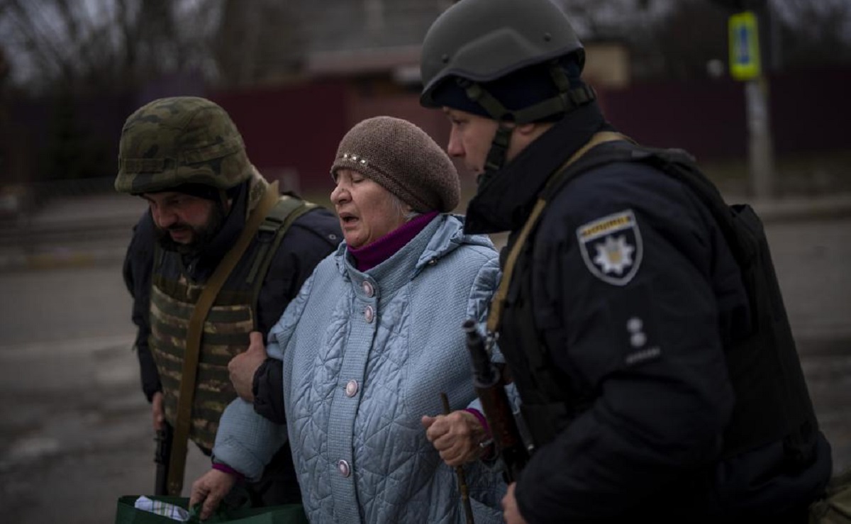 Ukrainian police officers help a woman fleeing as the artillery echoes nearby in Irpin, in the outskirts of Kyiv, Ukraine, Monday