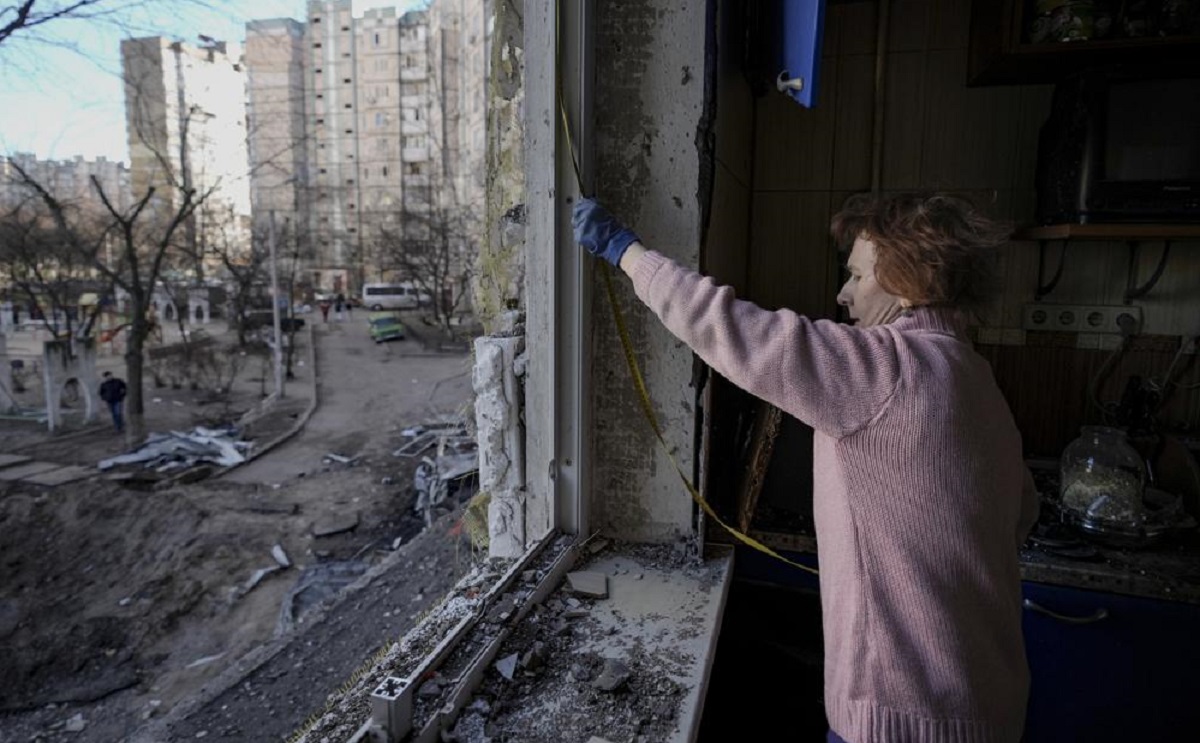 A woman measures a window before covering it with plastic sheets in a building damaged by a bombing in Kyiv, Ukraine