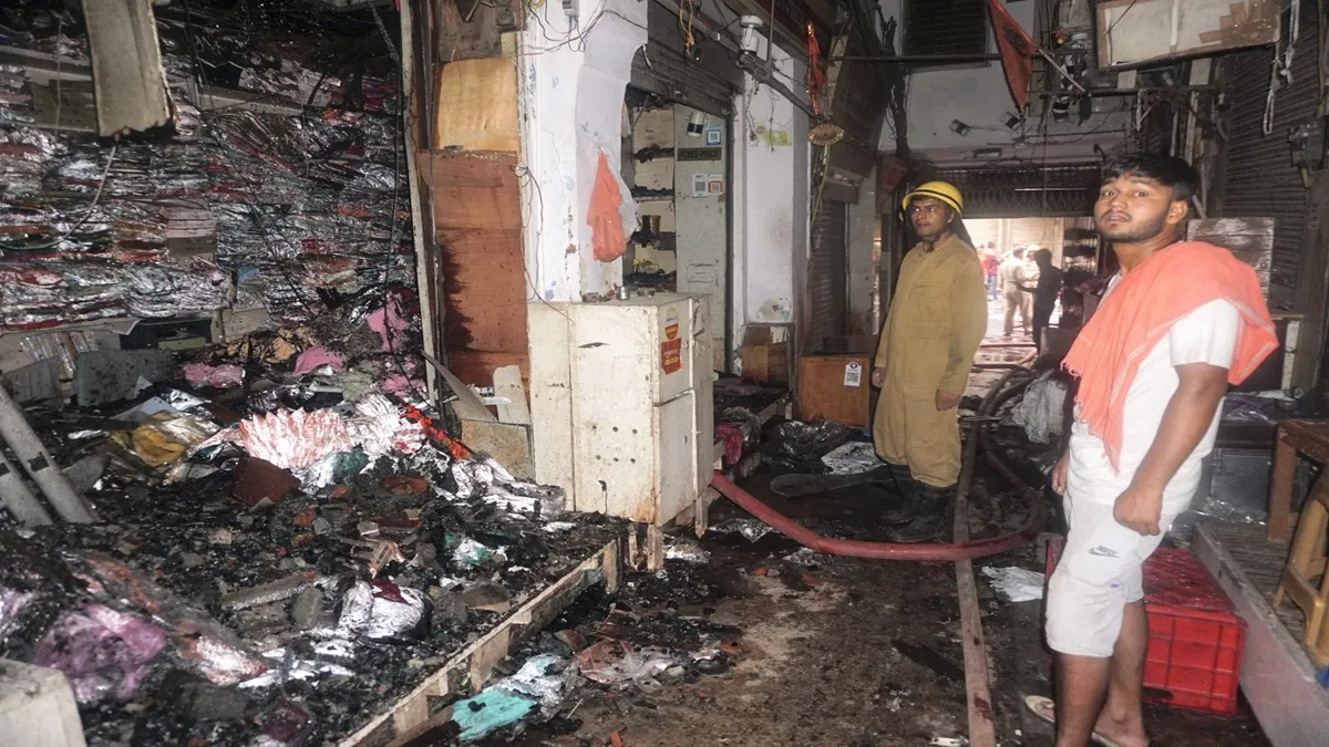 Firefighters and others stand near damaged shops after a fire broke out at Chandni Chowk 