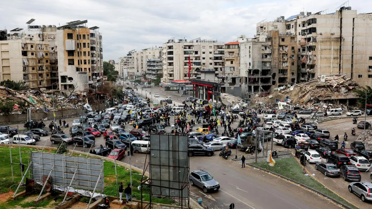 People gather as vehicles drive near damaged buildings, in Beirut's southern suburbs, after a ceasefire between Israel and Hezbollah took effect