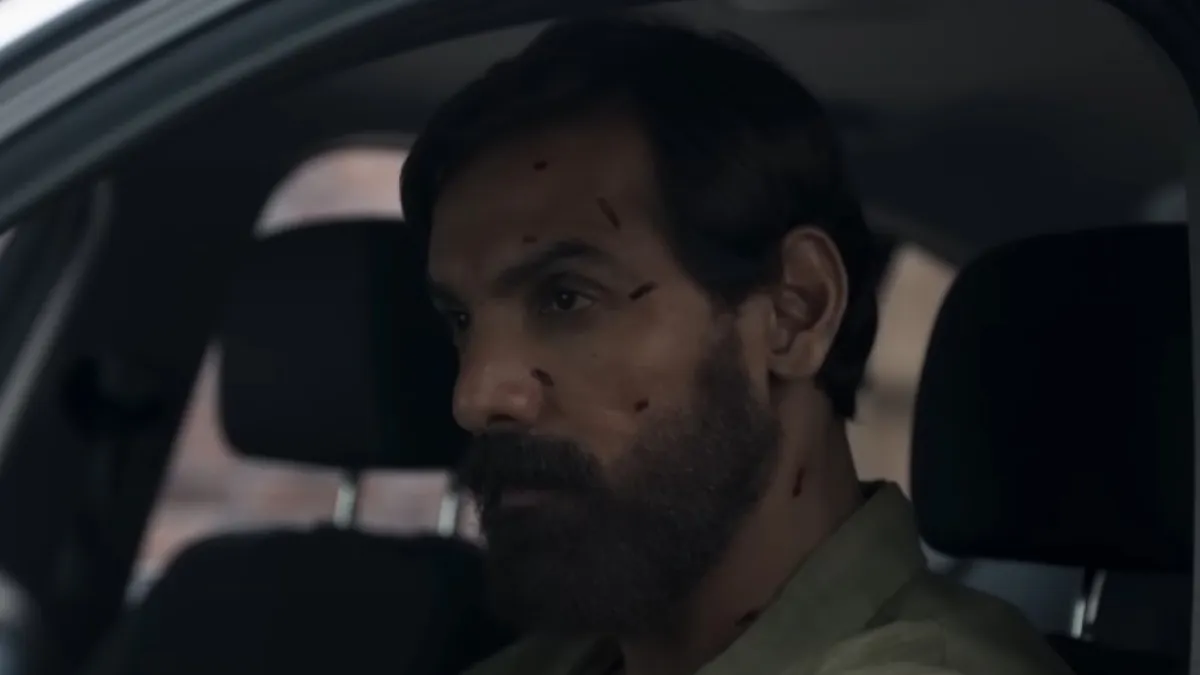 John Abraham in a gripping still from Tehran, streaming on Zee5 from August 14. John Abraham in a tense scene from Tehran, sporting a beard and minor facial injuries inside a car.