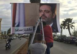 Workers hang a poster of outgoing PM Saad Hariri with Arabic words that read, “We are all Saad,” on a seaside street in Beirut, Lebanon