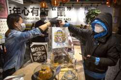 Manager Chen Tiantian, left, hands a takeaway order to a delivery driver at a Moka Bros cafe in Beijing, Friday, Feb. 14, 2020. For Valentine's Day Moka Bros, a health food eatery in Beijing, offered a special that included both a rose and a note logging the temperature of the chef that made the meal. Like many businesses in China, the restaurant has struggled to cope with the impact of a virus that has infected tens of thousands of people worldwide and sent several cities into lockdown. (AP Photo/Mark Schiefelbein)
?