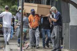 Cemetery workers carry the remains of a person in a cardboard coffin for burial at the General Cemet