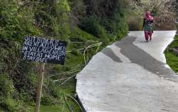 A sign at the entrance of a village reads 'Outsiders aren't allowed in Village Naddi - stay home-stay safe' as a woman walks out of Naddi village in Dharmsala, India. The new coronavirus causes mild or moderate symptoms for most people, but for some, especially older adults and people with existing health problems, it can cause more severe illness or death. (AP Photo/Ashwini Bhatia)