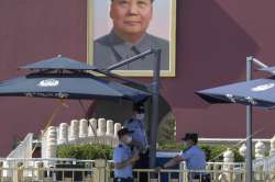 Chinese police officers wearing masks shelter in the shade near a portrait of Mao Zedong on Tiananme