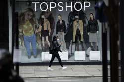 Woman wearing a face mask walks past mannequins wearing face masks in the window of a temporarily cl