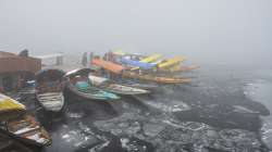 Boatmen stand near their Shikaras during a cold and foggy morning, in Srinagar