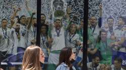 Two women walk past a Real Madrid poster of the team celebrating in a merchandising shop in Madrid, Spain, Monday, April 19