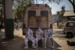 Exhausted workers, who bring dead bodies for cremation, sit on the rear step of an ambulance inside a crematorium, in New Delhi