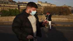 A man walks with a face mask to prevent the spread of the coronavirus, as a man takes a snapshot of the sunset, in Paris. 