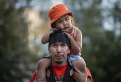 Cowichan Tribe member Benny George holds his child Bowie, 3, on his shoulders as they listen during a ceremony and vigil for the 215 children whose remains were found buried at the former Kamloops Indian Residential School, in Vancouver, British Columbia, on National Indigenous Peoples Day