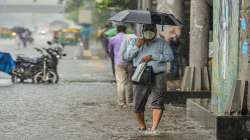 A man carries an umbrella as he walks on a waterlogged road during heavy rain.