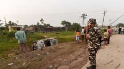 A security personnel stands guard while people take a look at the overturned SUV which destroyed in yesterdays violence during farmers protest, at Tikonia area of Lakhimpur Kheri district.