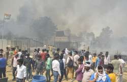 Locals look on as smoke billows from a fire in a slum area and a cow-shed nearby, at Indirapuram in Ghaziabad, Monday, April 11, 2022.