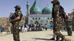 Men raise an Islamic flag during celebrations of Nowruz, the Persian new year, as Taliban soldiers stand guard at the Kart-e-Sakhi shrine in Kabul, Afghanistan, Monday, March 21, 2022. 