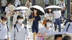 People, some of them holding parasols, cross an intersection amid heat, in Tokyo