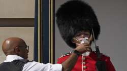 A police officer givers water to a British soldier wearing a traditional bearskin hat, on guard duty outside Buckingham Palace