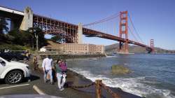 People walk along a seawall with Fort Point and the Golden Gate Bridge in the background in San Francisco.