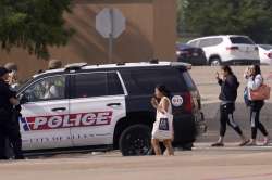 People raise their hands as they leave a shopping center after a shooting