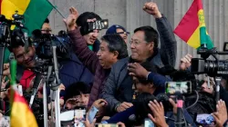 Bolivian President Luis Arce raises a clenched fist surrounded by supporters and media, outside the 