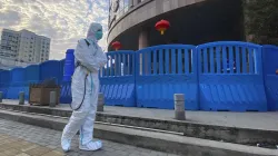 A worker in protectively overalls and carrying disinfecting equipment walks outside the Wuhan Centra