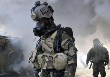 US soldiers wearing chemical warfare gear walk through smoke.