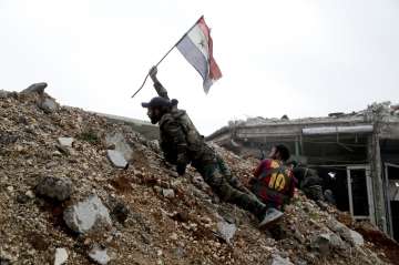 A Syrian army soldier places a Syrian national flag during a battle with rebels