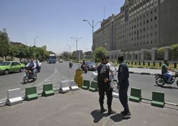 Police officers stand guard as vehicles drive past Iran’s parliament building