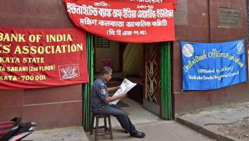 A security guard reads a newspaper in front of a closed bank in Kolkata