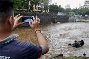 A man clicks picture of a car floating in a nullah in Mumbai on Wednesday