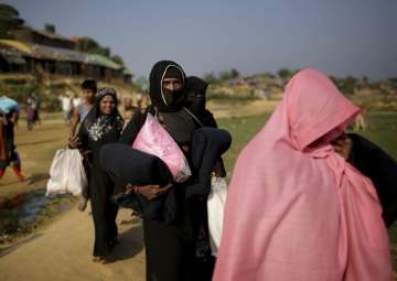 File - Rohingya Muslim women carry blankets and other supplies they collected from aid distribution centers in Kutupalong refugee camp in Bangladesh